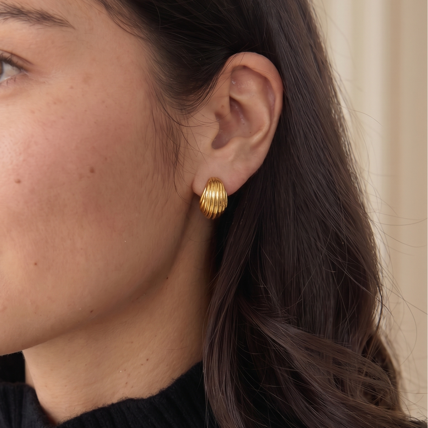 Close-up of a woman wearing gold earrings with a neutral background