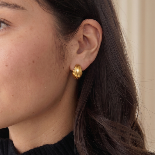Close-up of a woman wearing gold earrings with a neutral background